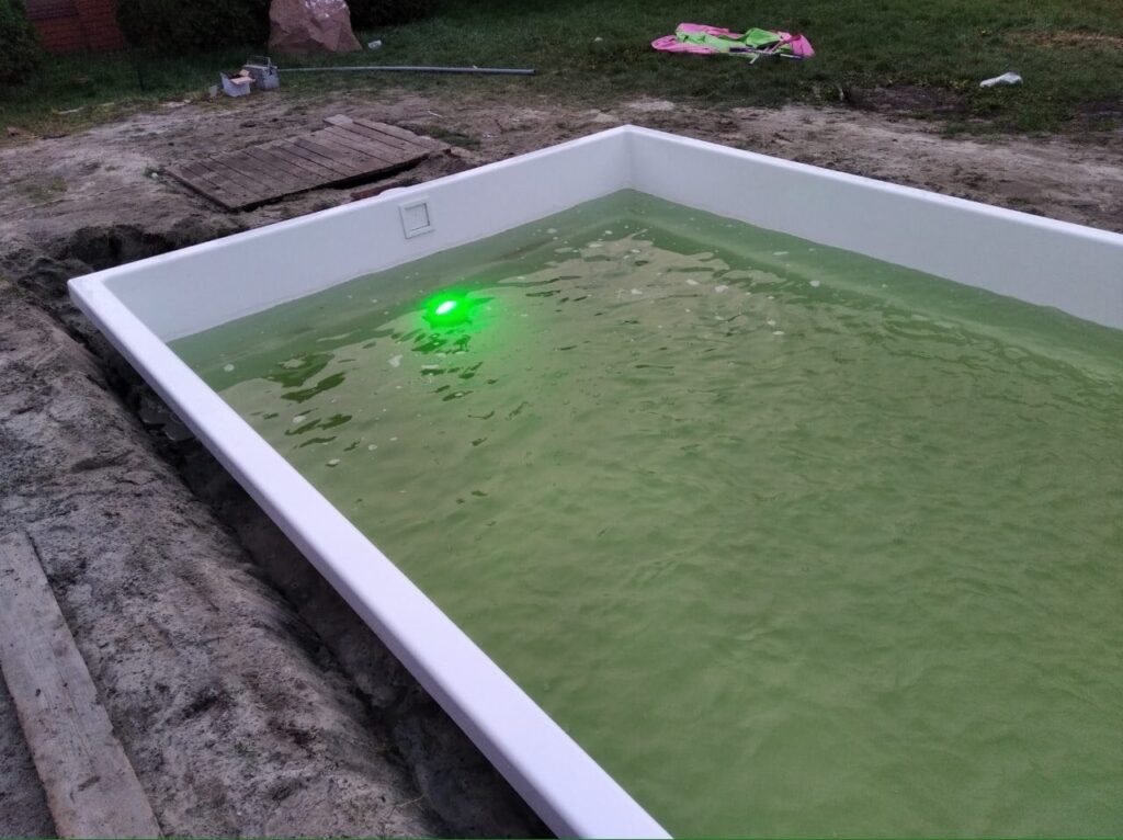 Зеленая подводная LED-подсветка в белом композитном бассейне во время вечернего тестирования систем.