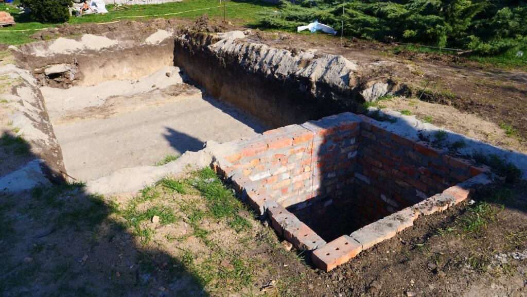 Крупный план котлована с песчаной подушкой и кирпичного технического помещения для фильтрационного оборудования бассейна — Grand Pools.