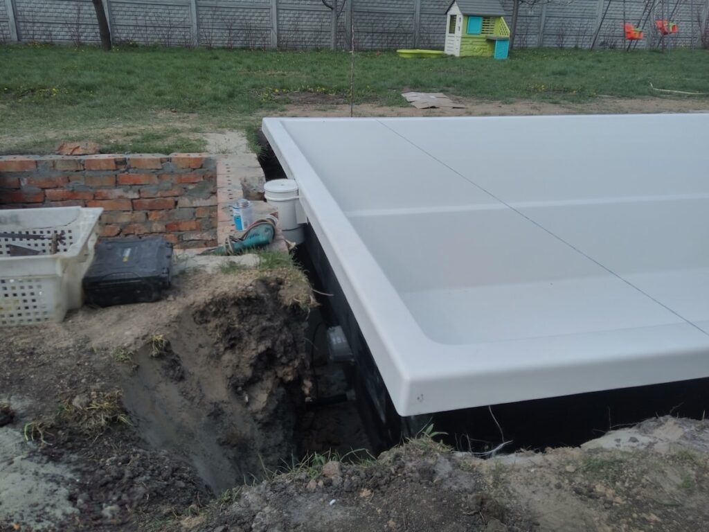 Білий композитний басейн на етапі монтажу з встановленим скімером та підготовленим цегляним приямком для обладнання.