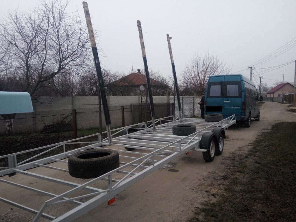 Спеціалізований фірмовий причіп для транспортування великих чаш, таких як композитний басейн, обладнаний вертикальними стійками та амортизаційними шинами.