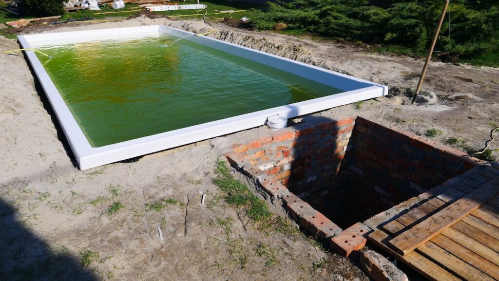 Біла чаша басейну Екліпс, що наповнюється водою в котловані поруч із спорудженням цегляного технічного приміщення.