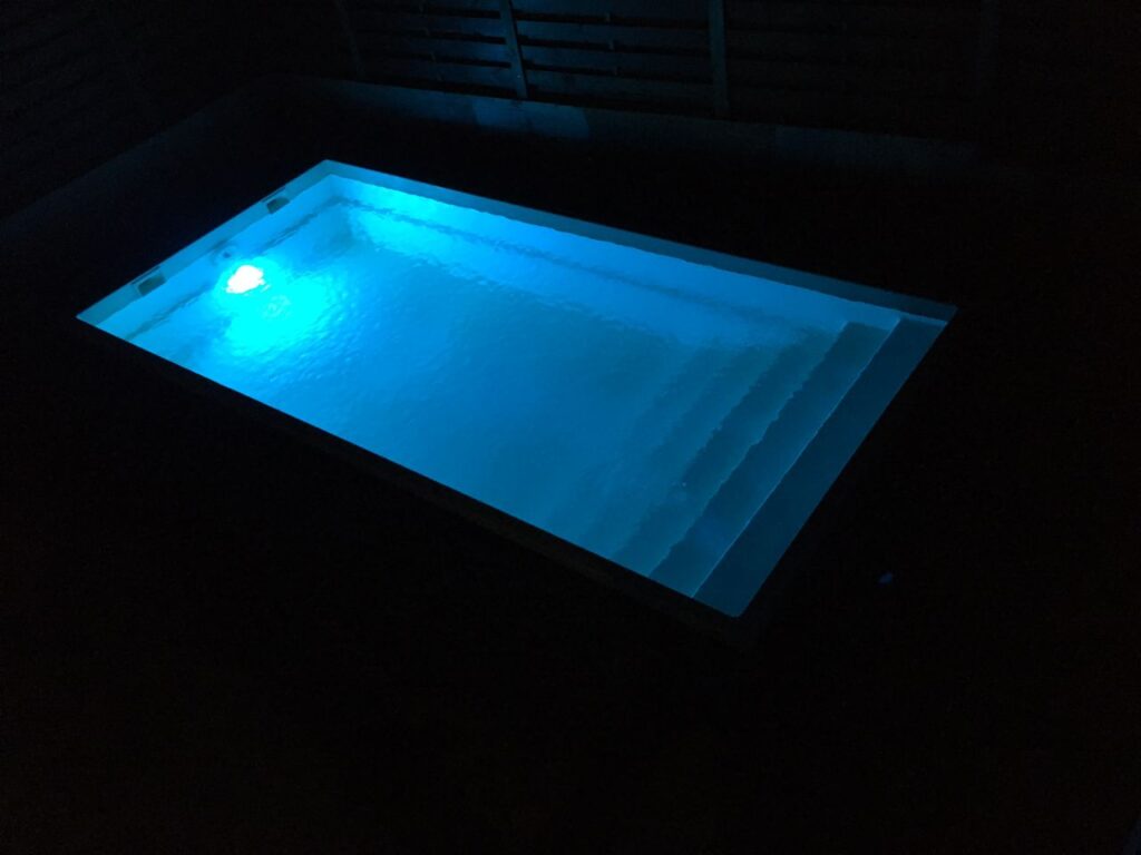 Ночной прямоугольный бассейн с яркой синей LED-подсветкой чаши и внутренних ступеней