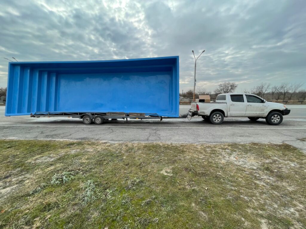 Синий композитный бассейн Эклипс 11 метров и коробки с оборудованием на прицепе во время транспортировки