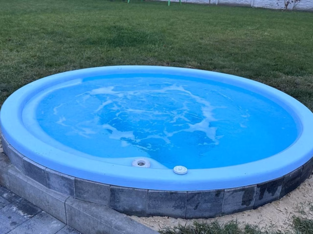 Синяя уличная купель с гидромассажем Grand Pools на фоне газона.