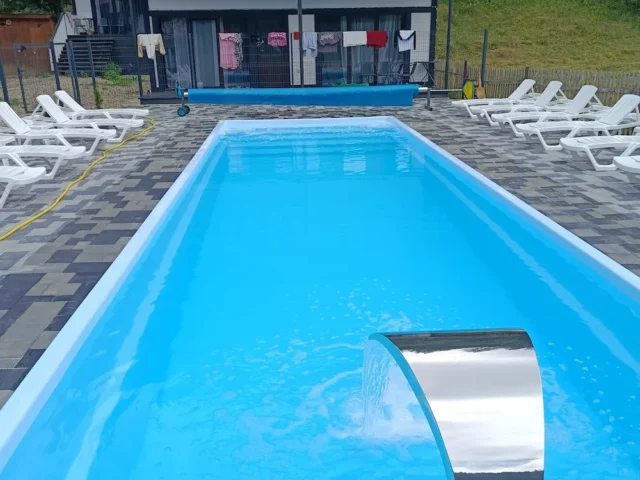 Композитний басейн Екліпс 11 метрів із водоспадом-каскадом і рядом шезлонгів на брукованому майданчику.