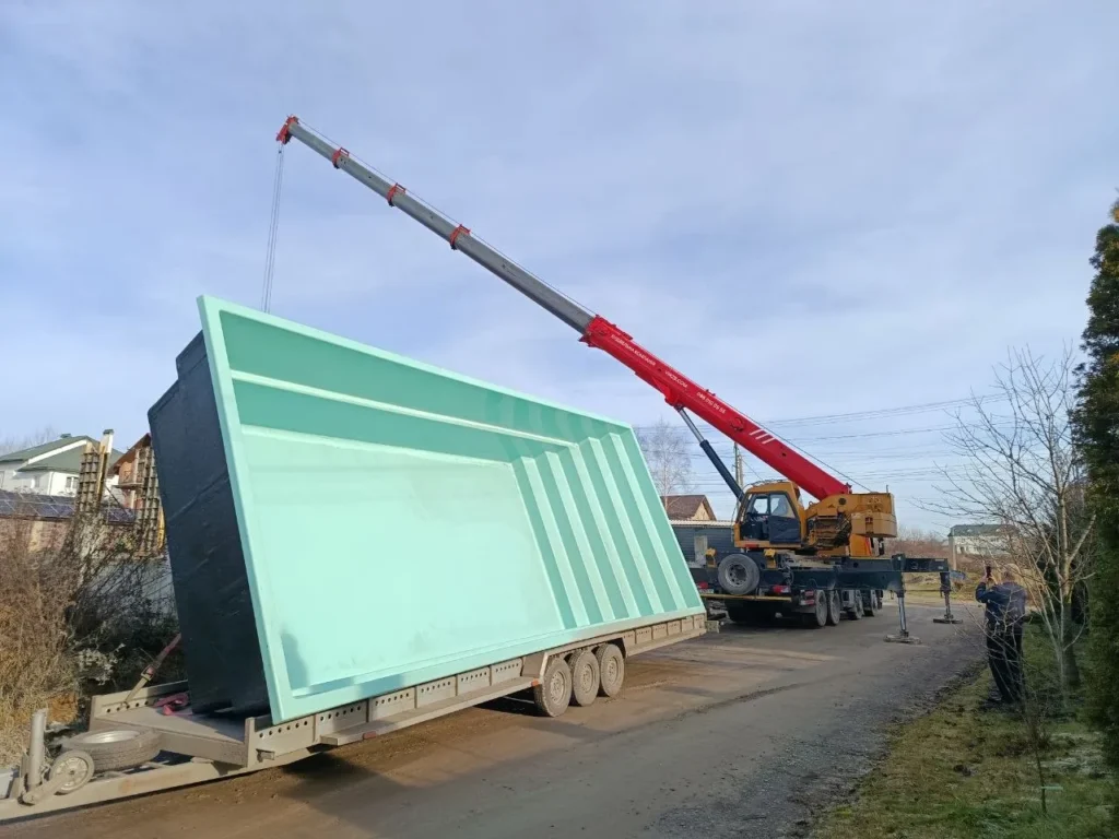 Разгрузка чаши композитного бассейна автокраном с прицепа на объекте.